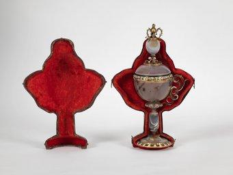 Anonymous, Case for the agate cup with one handle, seventeenth century. Madrid, Museo Nacional del Prado Kunstvoller Kelch aus Edelstein mit filigranen Verzierungen, präsentiert in einem offenen, roten Samtetui, das detailliert gestaltet ist.