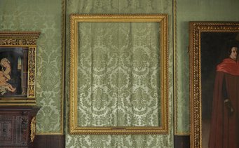 Isabella Stewart Gardner Museum. Photo by Sean Dungan An empty gold frame hangs against green patterned wallpaper, flanked by two paintings.